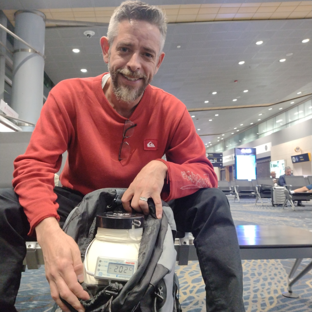 Photo of a courier smiling to the camera as he holds a dewar flask during the transportation process.